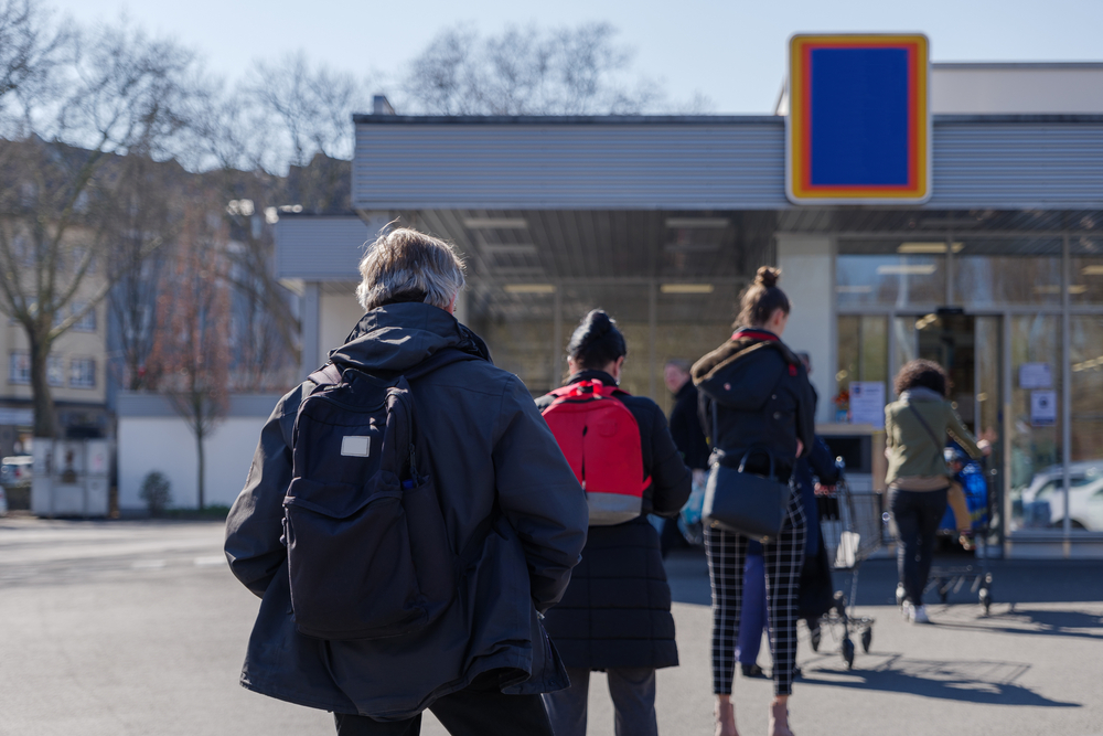 European people queue on street outside supermarket during quarantine for COVID-19 virus in Düsseldorf, Germany. Image by Peeradontax / Shutterstock. Germany, 2020. European people queue on street outside supermarket during quarantine for COVID-19 virus in Düsseldorf, Germany. Image by Peeradontax / Shutterstock. Germany, 2020.