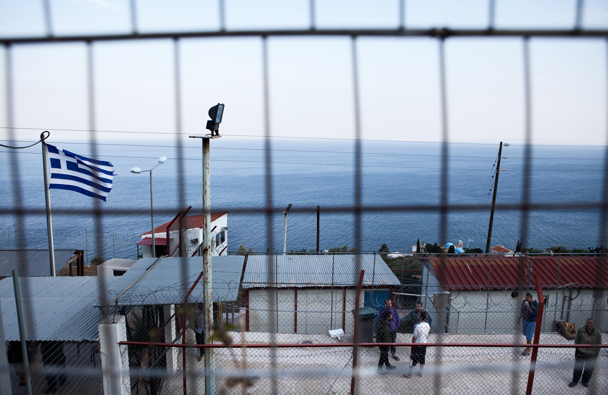 Police holding camp for undocumented migrants on Chios Island, Greece, Oct. 4, 2014. After the Coast Guard has processed new arrivals, Syrian asylum seekers will spend a few days, or sometimes longer, locked in this detention camp while the police complete the paperwork for a temporary stay in Greece. Image by Holly Pickett. Greece, 2014.