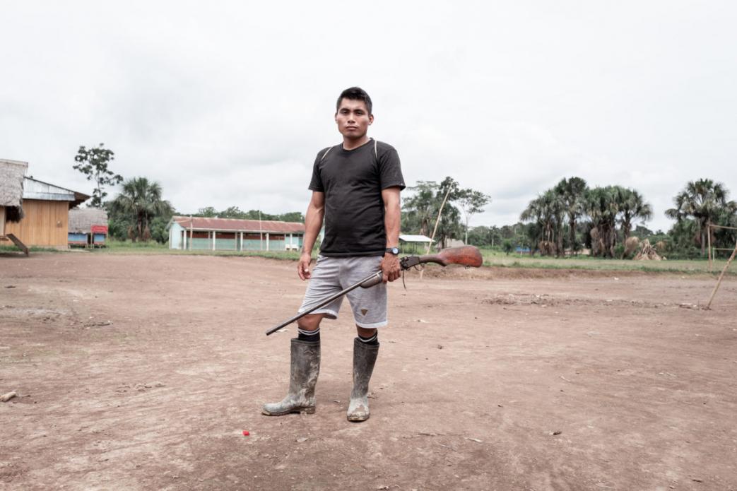 Man standing with gun. Image by Marcio Pimenta. Peru, 2019. Man standing with gun. Image by Marcio Pimenta. Peru, 2019.