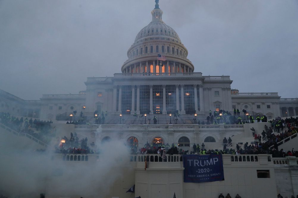 Rioters rush the front steps of the U.S. Capitol building with the dome in the background.