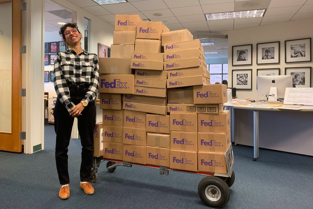 An intern stands with a pallet of 1619 magazine copies to be shipped to schools.