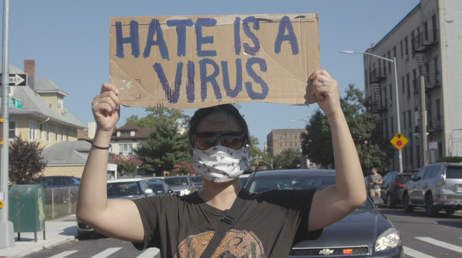 A masked person holds a sign that reads 'hate is a virus'