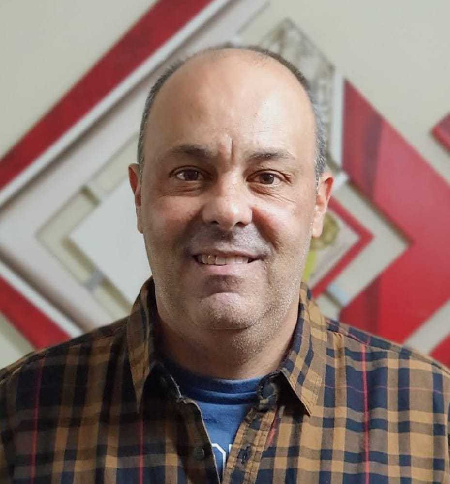 A man wearing a yellow stripe flannel shirt smiles at the camera.