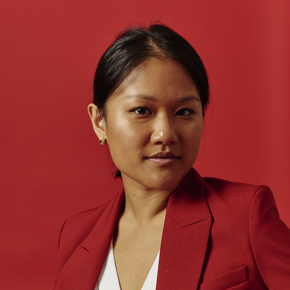 Headshot of woman in red jacket against a red backdrop