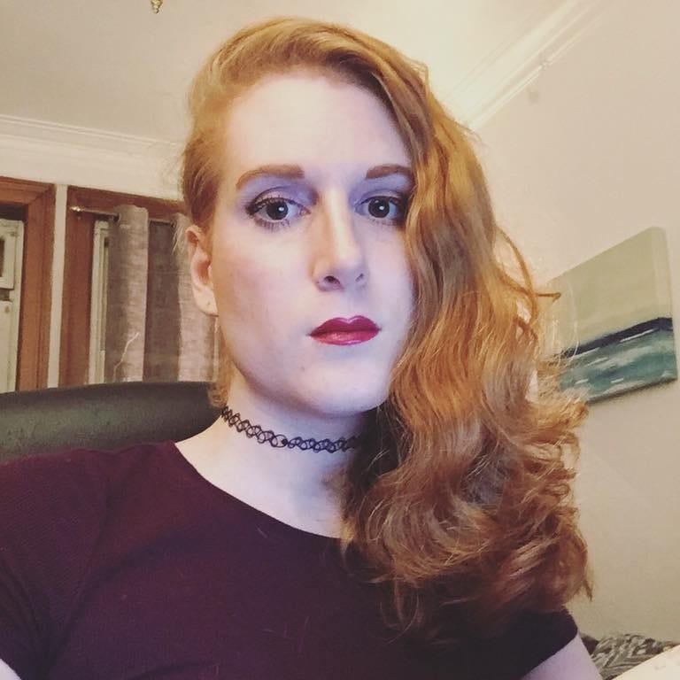 A person with long red hair wearing a maroon t-shirt
