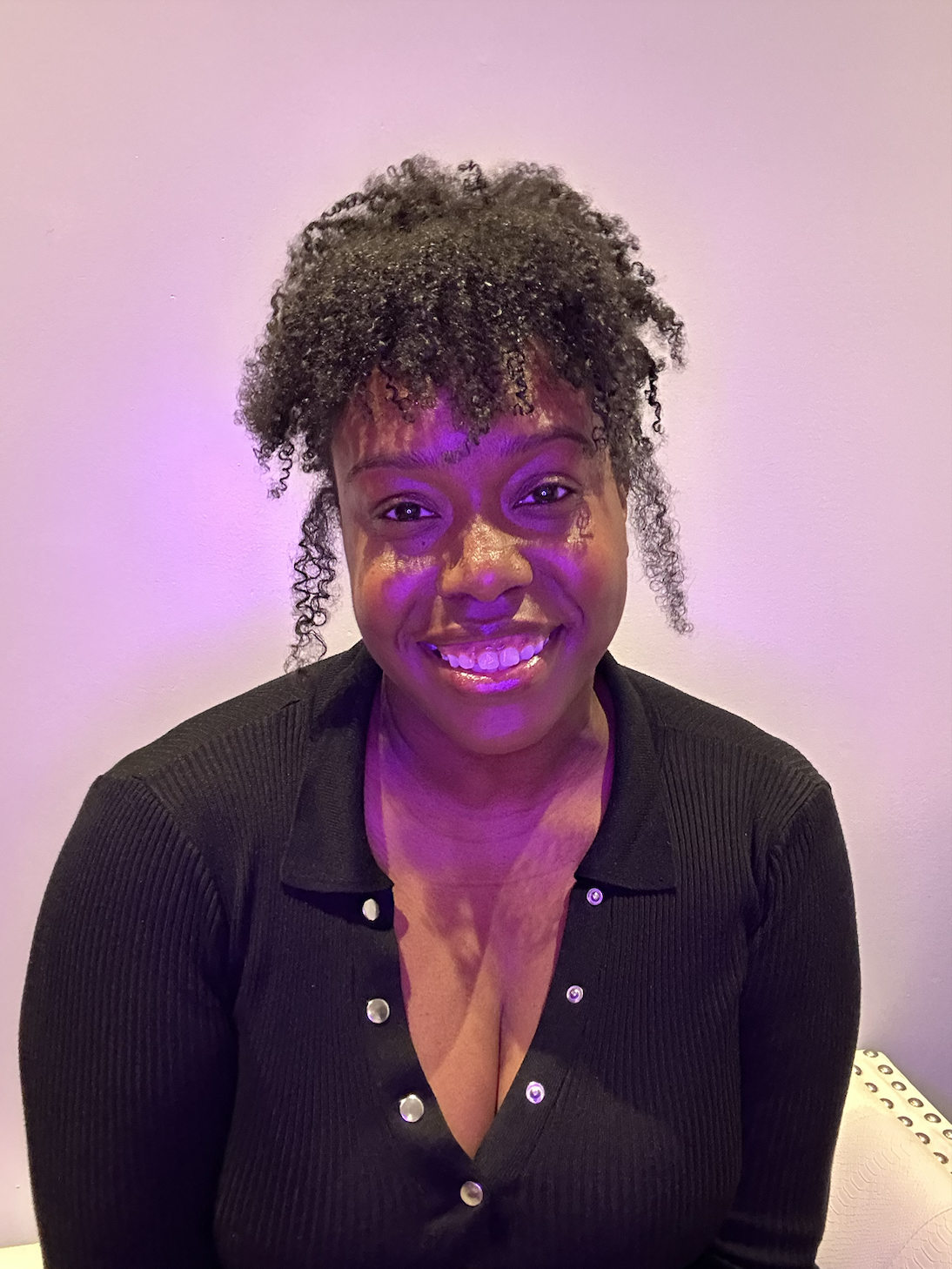 Shauntice, a Black woman with her curls in an up-do smiles at the camera