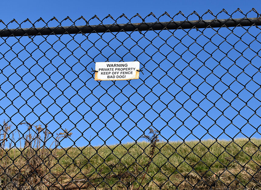 Image of a black chain-link fence with a sign that reads "Warning, private property, keep off fence, bad dog!"