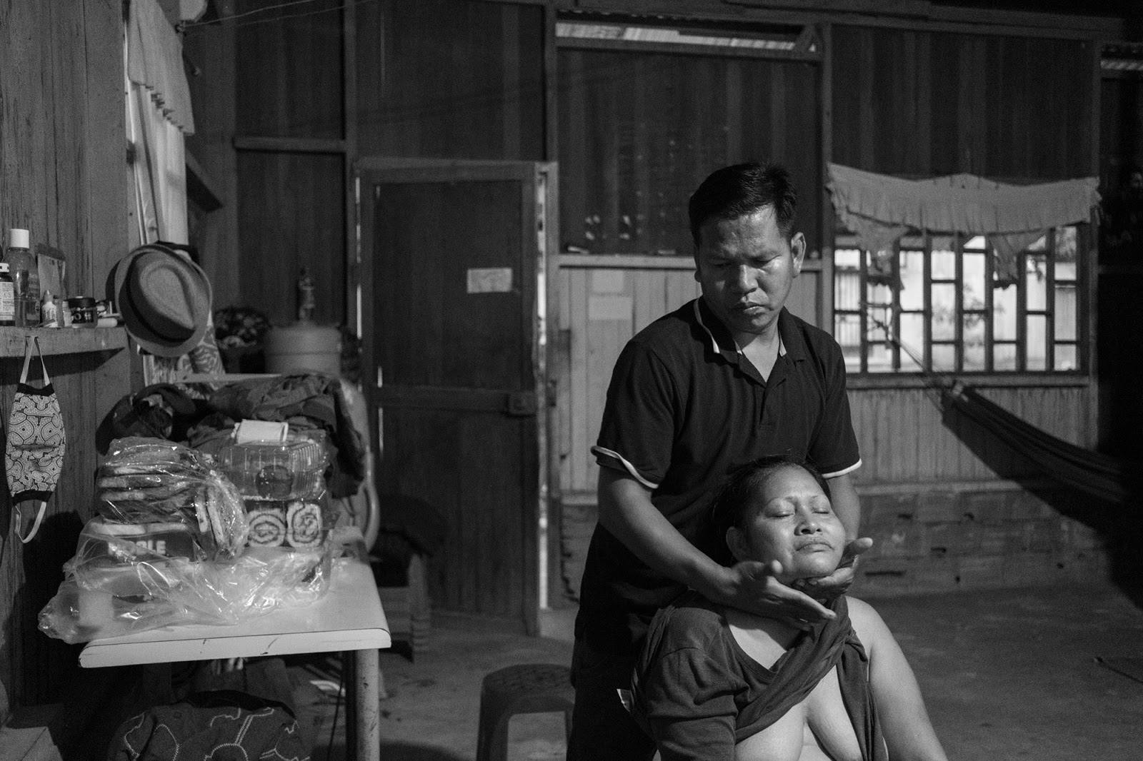 A man is standing behind a seated woman and his hands hold her chin up.