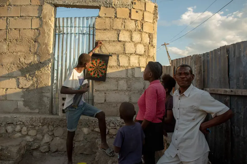 Alisma Robert, right, and children Esaie Robert, 15, Roberson Robert, 7, and Kerline Reobert, 18, standing, enjoy the evening at their home in the Canaan 3 neighborhood of greater Canaan, Haiti, January 7. Thomson Reuters Foundation. Image by Allison Shelley. Haiti, 2019.