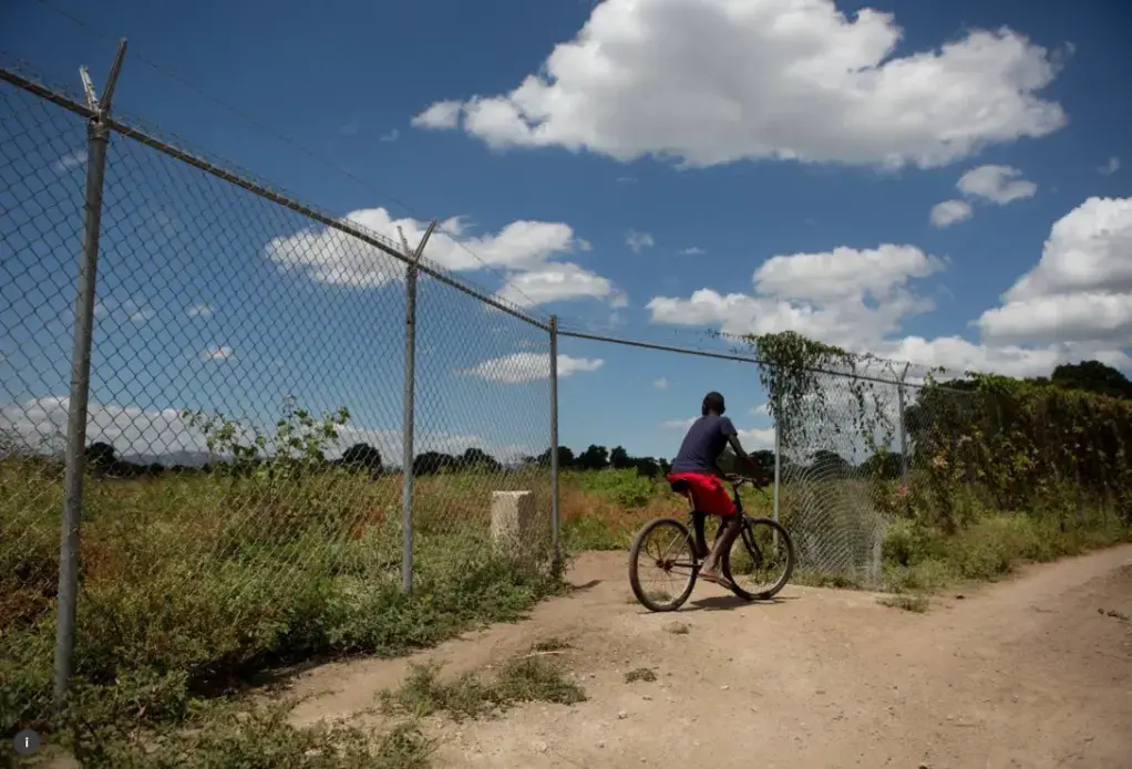 A boy rides past fenced off land in the north of Haiti, April 14, 2015. Much of the area land was appropriated from local farmers to build the nearby Caracol Industrial Park. Image by Allison Shelley. Haiti, 2015.