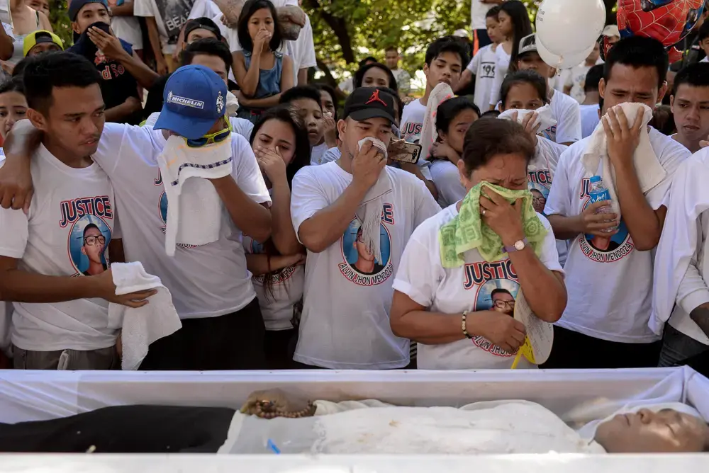A family and friends of the deceased grieve standing before an open casket.