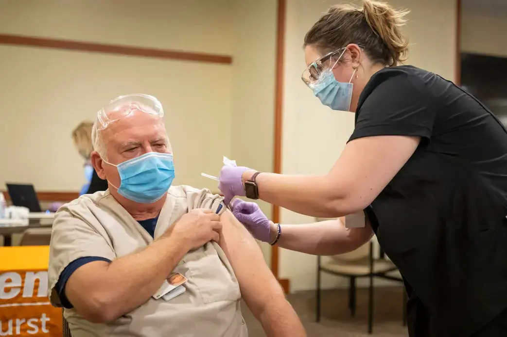 Register Nurse and Infectious Control Specialist Sarah Czechowicz administers the first COVID-19 vaccine at Elmhurst Hospital to Edward Sulita a Transporter at the Hospital on December 12, 2020. Image by Manuel Martinez / WBEZ. United States, 2020.