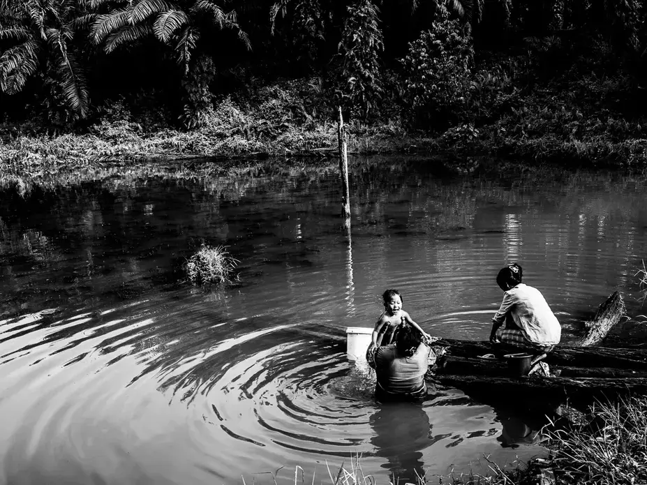 WATER SOURCE.&nbsp;Santi takes a bath in the murky water with a neighbor while her mother Ida washes their clothes. The reservoir is the community's only source of water. Image by Xyza Cruz Bacani. Indonesia, 2018.&nbsp;
