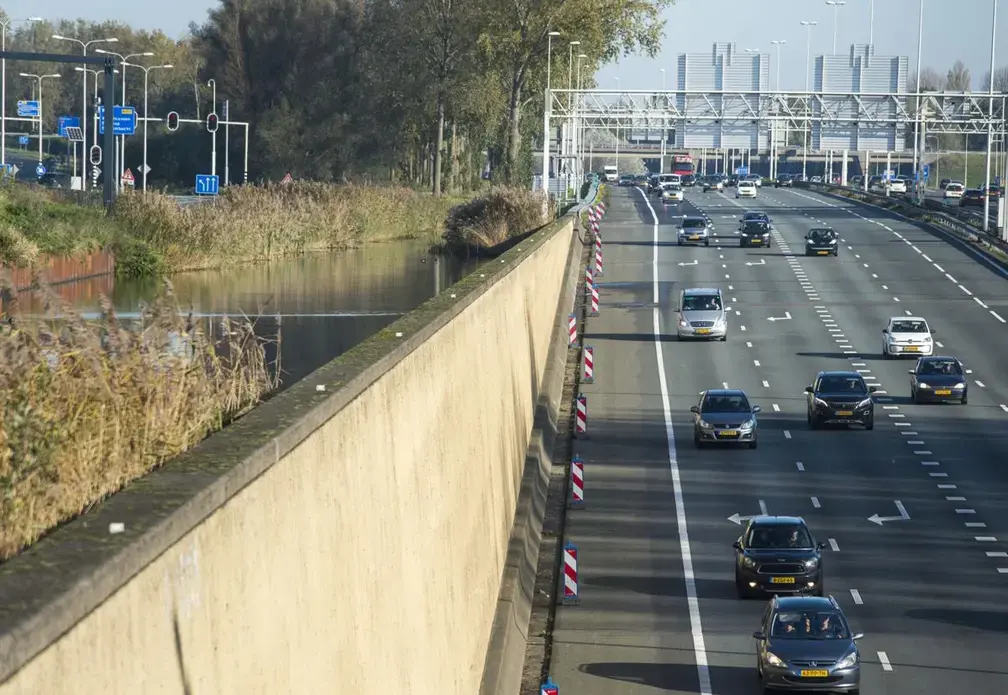 A large wall holds back water, left, as cars on an highway drive under an approaching canal near Rotterdam. Image by Chris Granger. Netherlands, 2019.