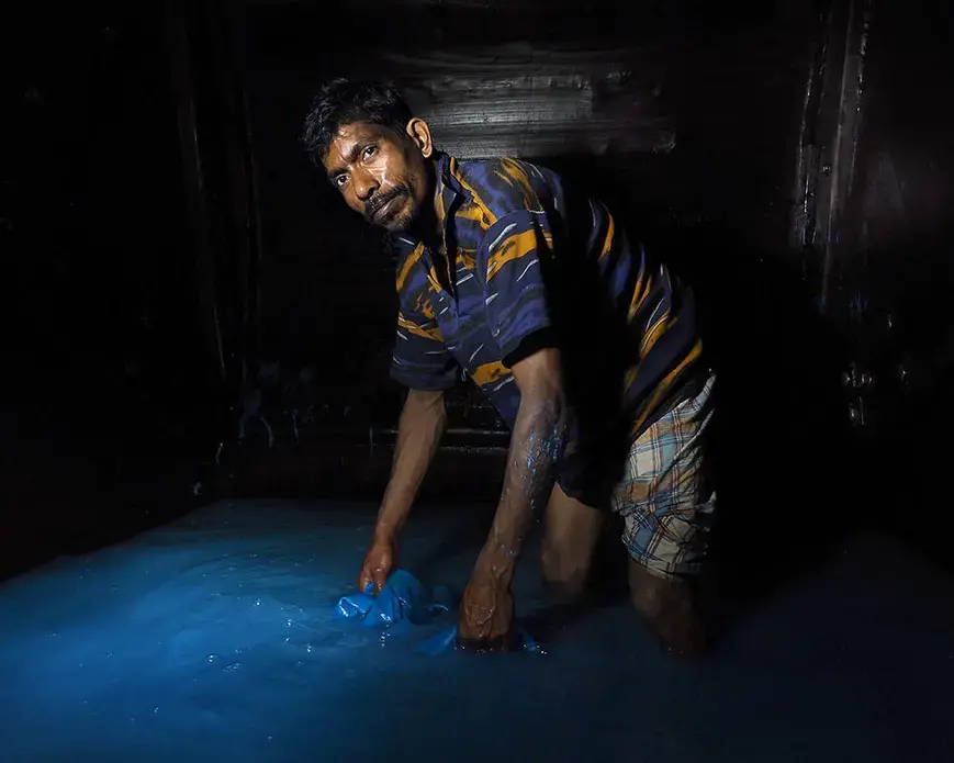 A barefoot worker stands inside an 8-foot tall-tumbling drum filled with chromium (III) sulfate and other chemicals. Workers often have to crawl inside the drums to remove hides. Image by Larry C. Price. Bangladesh, 2016.