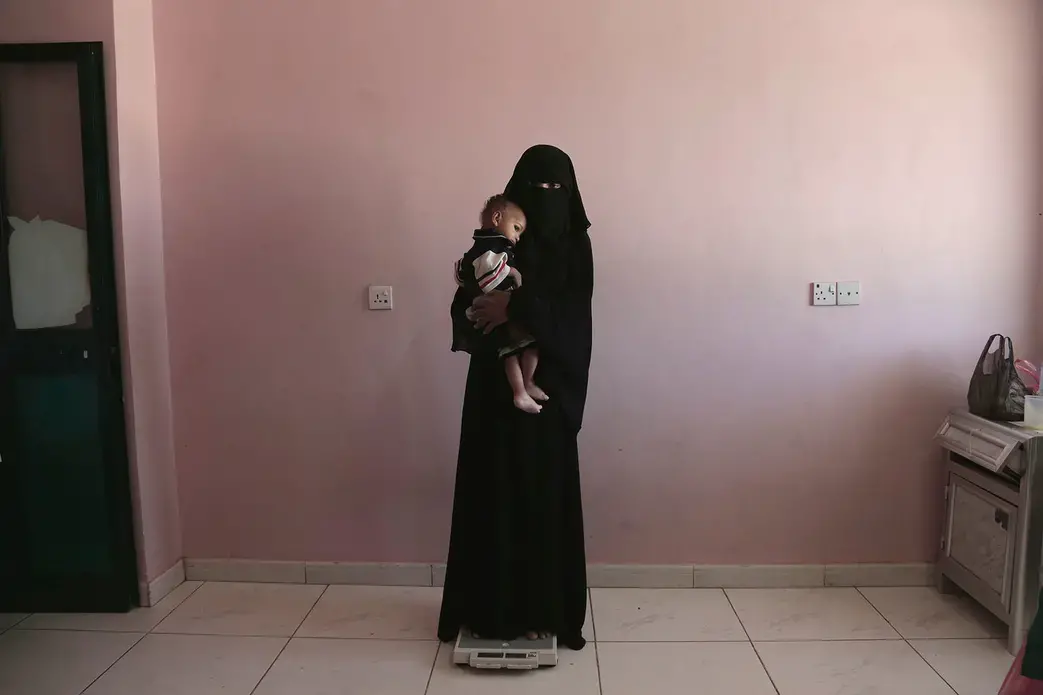 Umm Mizrah holds her baby Mizrah, in Aden, Yemen. Image by Nariman El-Mofty. Yemen, 2018.