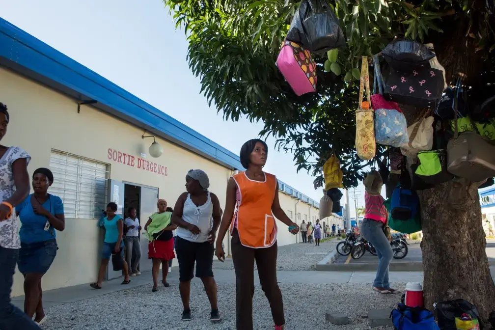 Workers retrieve lunch satchels left hanging in trees outside of a Sae-A Trading Company factory building at the Caracol Industrial Park in the north of Haiti on April 14. Sae-A is the anchor tenant of the $300 million-park, employing about 5,000 workers—still far short of the 60,000 jobs originally projected by 2017. The Clintons were instrumental at nearly every step in its creation. Image by Allison Shelley. Haiti, 2014.