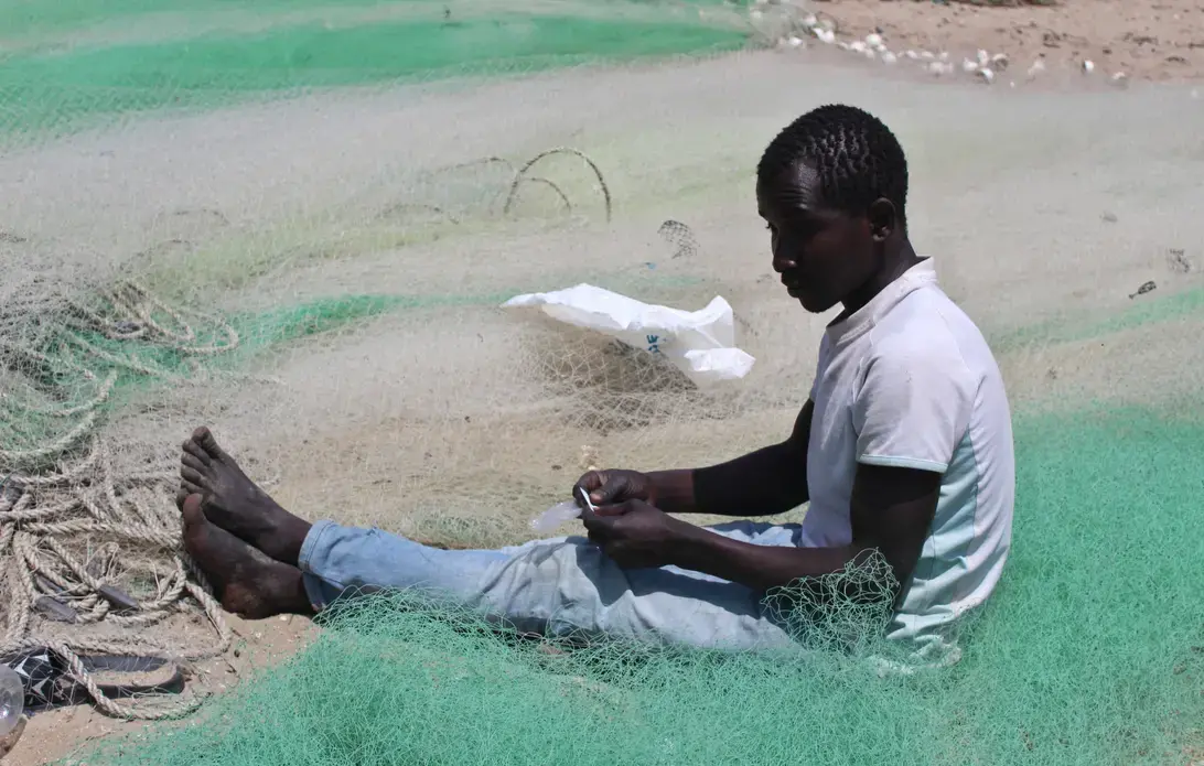 A fisherman mends his net on the beach at Gunjur fishing village. Image by Nosmot Gbadamosi. The Gambia, 2018.