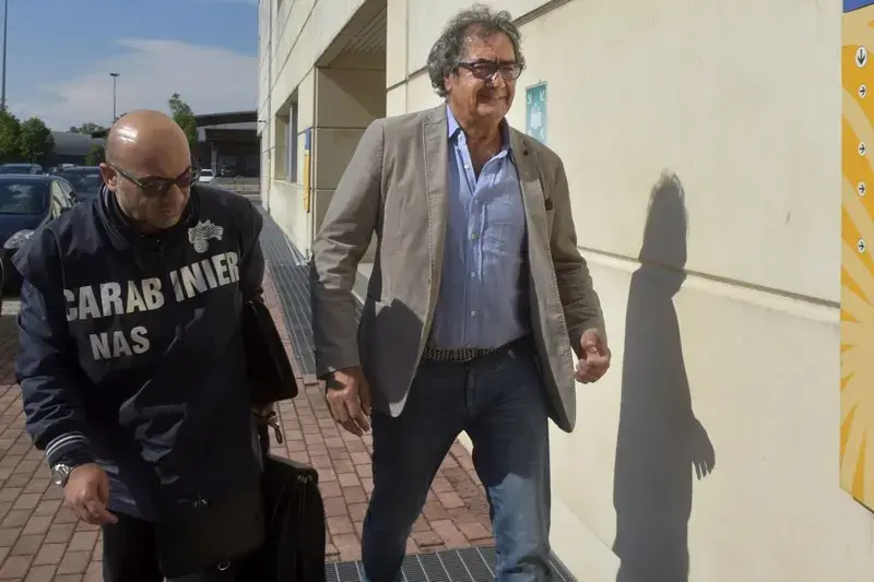 Dr. Guido Fanelli, right, is taken to the Carabinieri headquarters in Parma, Italy, for questioning in an alleged pharmaceutical kickback scheme on Monday, May 8, 2017. That morning, police jolted Fanelli out of bed. It was a spectacular fall from grace for a man who appeared days before on a popular television show to promote painkillers. Image by AP Photo/Marco Vasini. Italy, 2017.