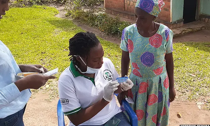 Officials from EPHWOR give out birth control pills to a woman in Buhweju district. Image by Fredrick Mugira. Uganda, undated.