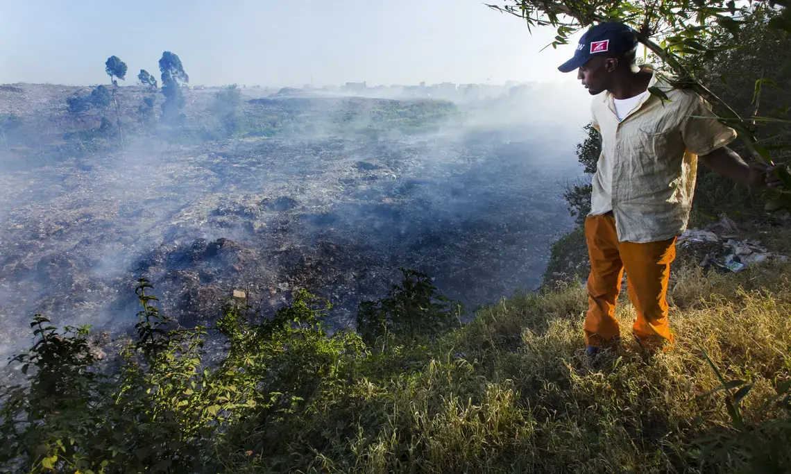 A man stands on the edge of a precipice overlooking Dandora, Korogocho’s 30-acre massive dump of smoldering garbage. People scavenge through the dump looking for anything of value. Image by Mark Hoffman. Kenya, 2017.