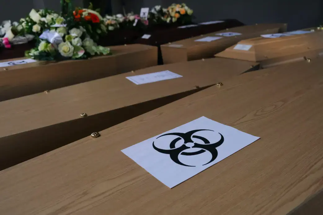 Coffins of COVID-19 victims are marked with a "biohazard" warning sign as they are placed next to each other at the Pompes Funebres Fontaine funeral service company in Gilly, Belgium. Image by Alexandros Michailidis / Shutterstock. Belgium, 2020.