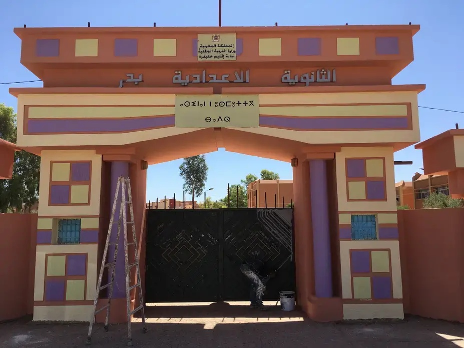 Workman adds finishing touches to the entrance to a Moroccan middle school. Morocco's new Minister of Education, Mohamed Hassad, has begun his tenure with a focus on achieving immediate results in advancing an ambitious program of reform, including significant changes to Morocco's language education policies. Another initial measure he took was to order all primary and middle schools to be repainted in bright pastels for the beginning of the school year, pictured here. Image by Gareth Smail. Morocco, 2017.
