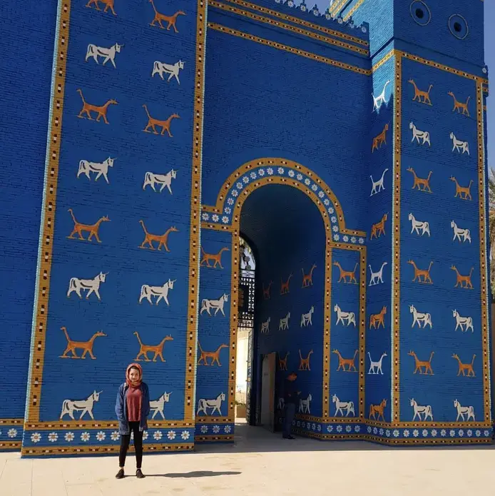 Zahra Ahmad, 24, stands in front of the blue wall leading into the ancient kingdom of Babylon, Iraq in Feb. 2019. Image courtesy of Ahmad family. Iraq, 2019.