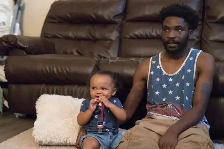Theron Carson sits on the floor with his daughter watching cartoons. Carson was charged with trafficking marijuana and had $1,200 seized from his home after the police smelled weed coming from his Newburg apartment and conducted a search. Image by J. Tyler Franklin. United States, 2019.