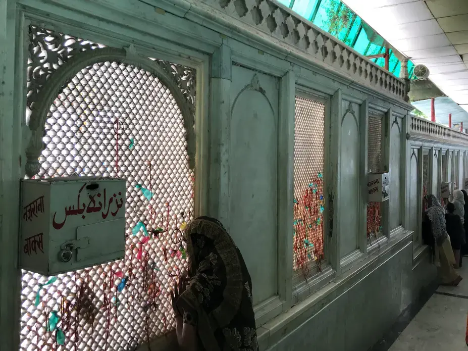 Women look through the jaali surrounding the courtyard of the dargah of Qutubuddin Bakhtiyar Kaki in Delhi. Image by Nikhil Mandalaparthy. India, 2019.