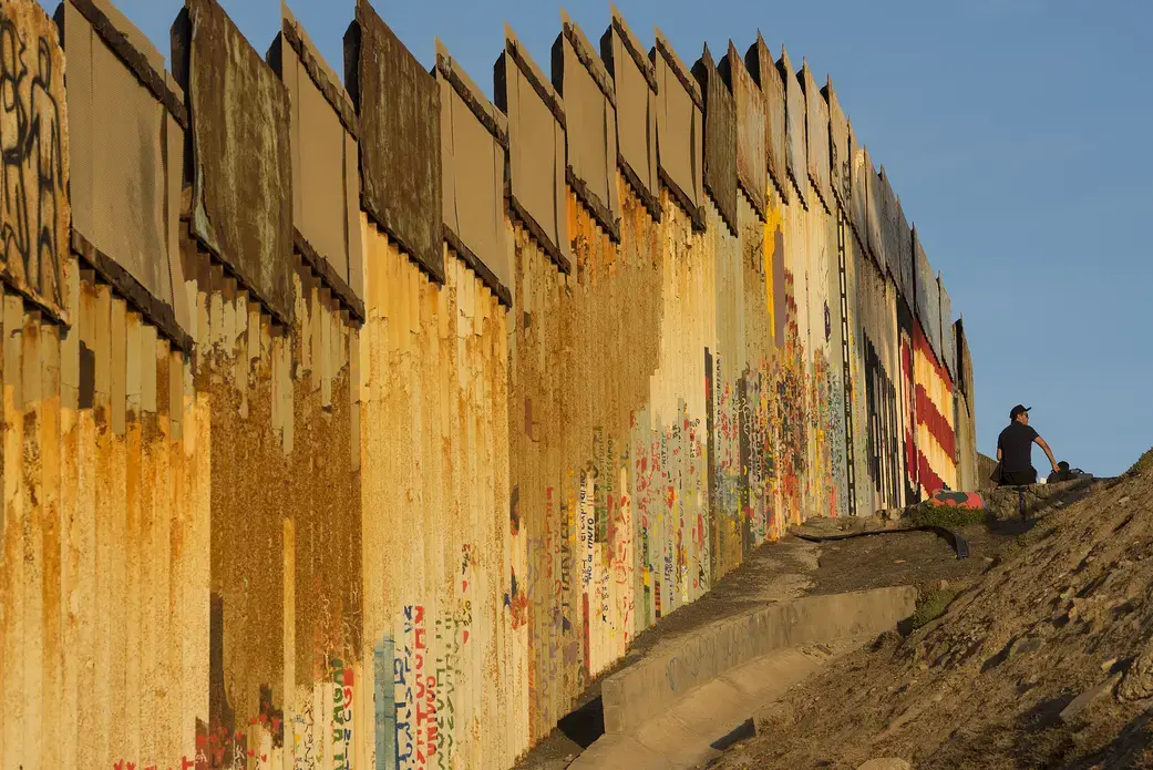A man sits by the border wall at Friendship Park as the sun sets over Playas de Tijuana on Dec. 1. Image by Amanda Cowan. Mexico, 2019.