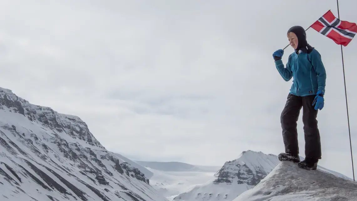 A child carries a Norwegian flag on a high Arctic landscape. Image by Amy Martin. Norway, 2018.