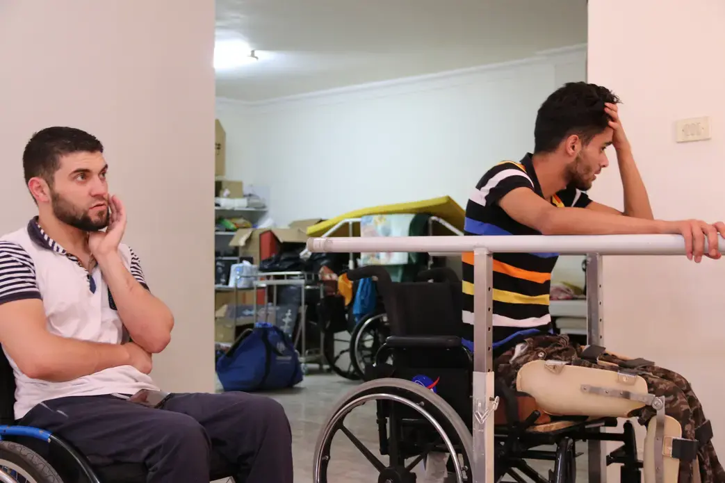 Obada Alasmi sits in on Mohammed Ayyash's training session. Ayyash is confined to a wheelchair,, but they discuss the possibility of using a walker in the near future. Image by Sawsan Morrar. Jordan, 2017.