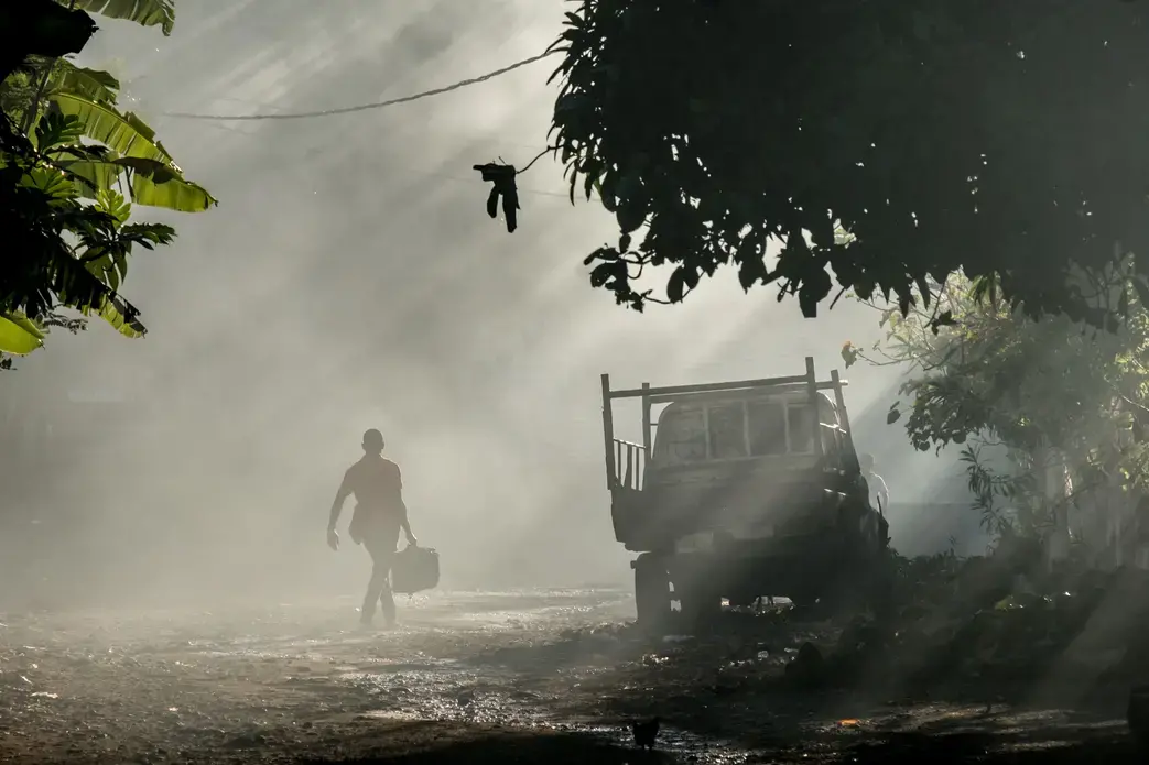 A man walks through clouds of smoke from burning rubbish in the village of Ouani, Anjouan, a popular departure point for Comorian migrants leaving for Mayotte. Image by Tommy Trenchard. Comoros, 2019.
