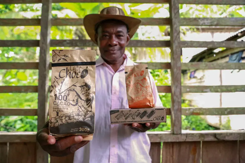 José Palacios, a cacao farmer, holds the Late Chocó chocolate products produced by his son, Joel, in Bogotá. The package bears an illustration of his likeness. José Palacios lives in Colombia's western Chocó department, which is also a coca-growing region. Image by Verónica Zaragovia. Colombia, 2018.