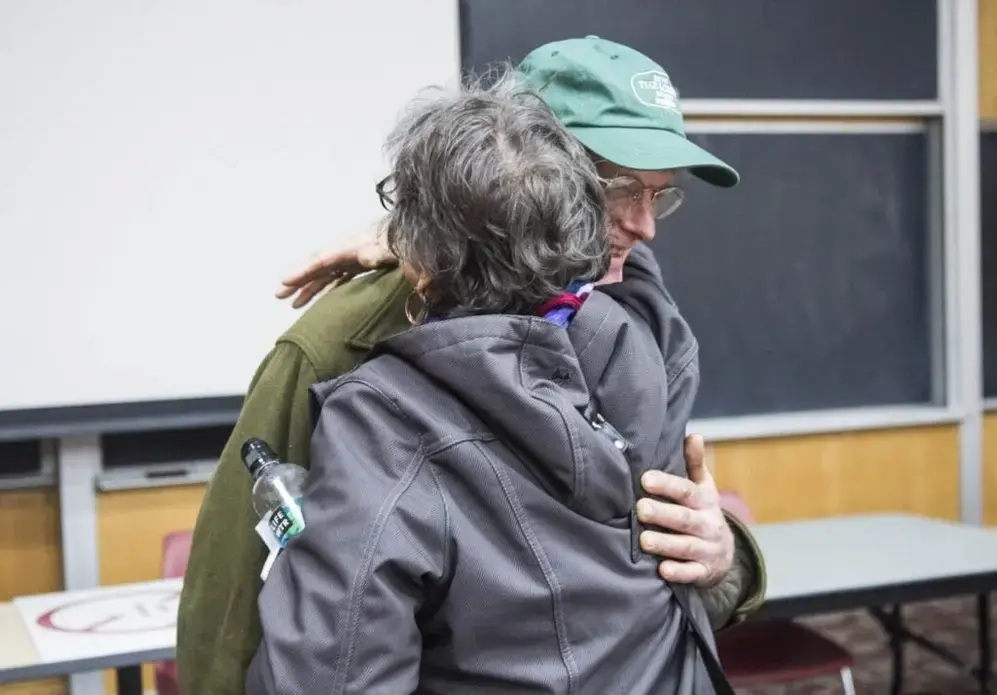 Duane Hanson embraces Roberta Benefiel-Frampton, director of the Grand River Keepers in Happy Valley-Goose Bay, Labrador, after a panel discussion at Preble Hall at the University of Maine in Farmington on Nov. 25, 2019. Image by Michael G. Seamans. United States, 2019.