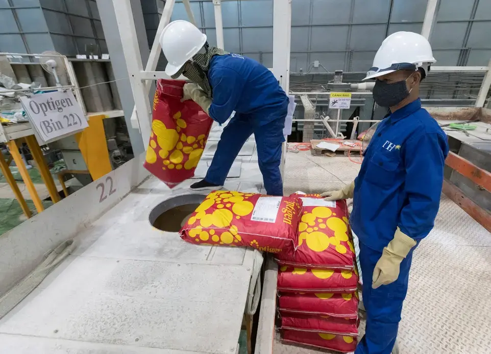 Workers empty bags of a nutritional supplement made by Alltech that will be blended with animal feed at TH Milk's operations in Nghia Son, Vietnam. The company has 200 workers dedicated to producing 500,000 tons of feed per year for its herd of 40,000 cows. Image by Mark Hoffman. Vietnam, 2019. 