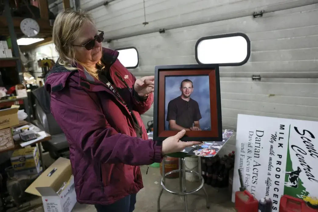 Amy Fischer is seen with a photo of her son, Brian, on her family’s 350-cow dairy farm, Darian Acres, in Rio, Wis., on Dec. 18, 2020. Brian died by suicide at the age of 33, on Dec. 21, 2016. The Fischers attribute his death to a combination of stress from work, a drinking problem and depression from a recent break-up. Dairy farmers and their advocates say numerous stressors are leading to a mental health crisis in their industry, including financial pressures, long hours, labor shortages and harsh weather.