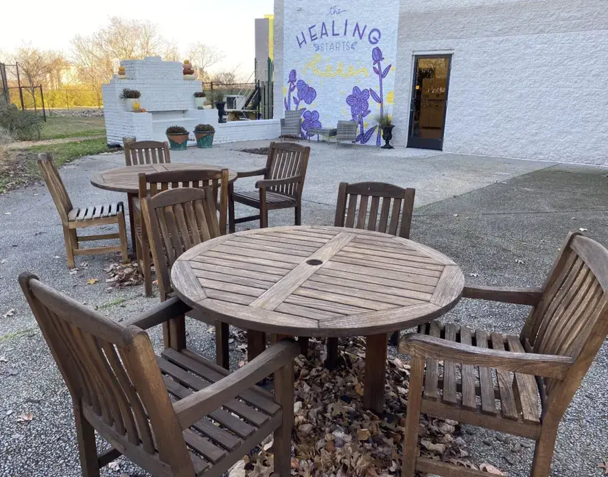 An outdoor space with sets of tables and chairs with potted plants. A mural on a wall reads, "The healing starts here."