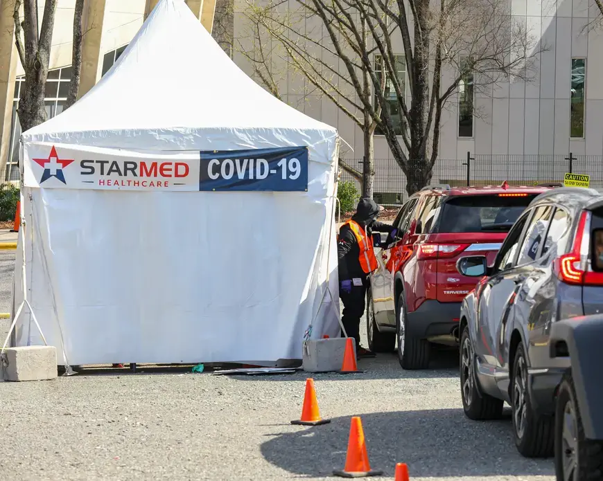 Vehicles line up next to a white tent that has a banner reading, "Starmed Healthcare COVID-19."