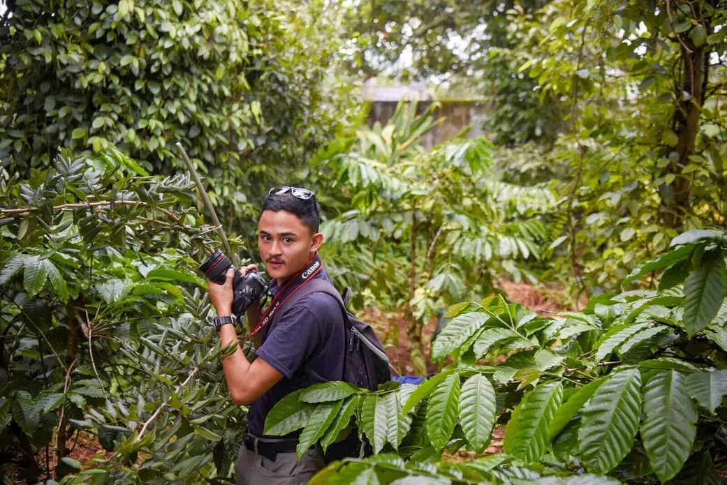 Anton Delgado stands in a forest holding a camera.