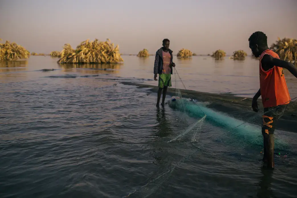 Two men stand in calf-deep water holding a fishing net at dusk