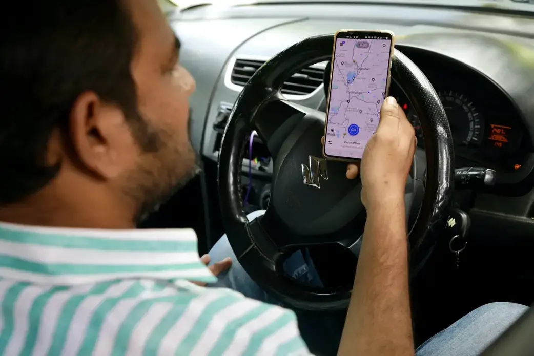 An uber driver checks the map on his phone while sitting at the wheel.