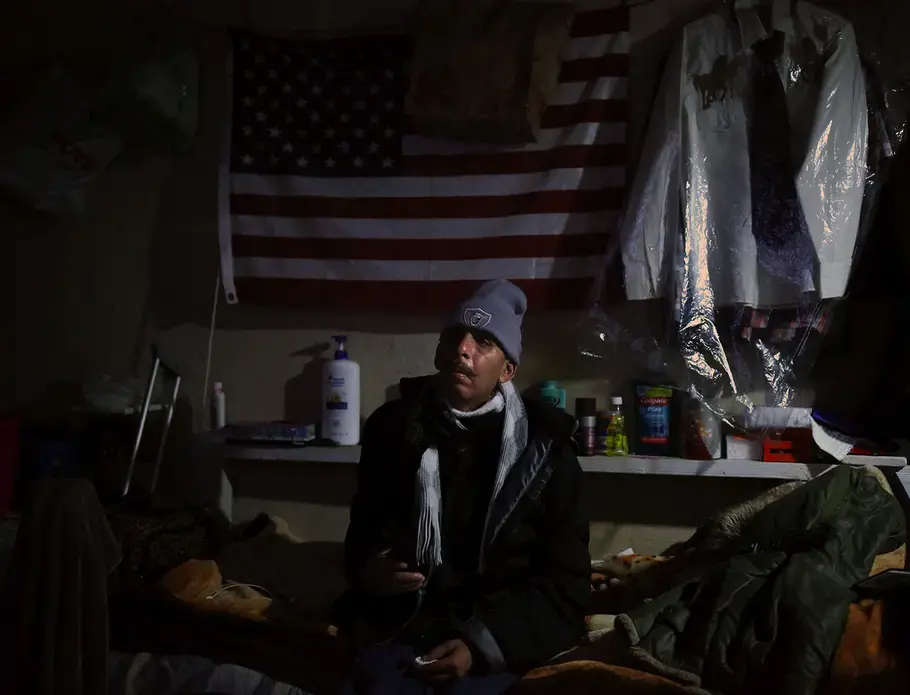 Roman watches TV at a Tijuana shelter for migrants, asylum-seekers and deported people. The shelter supports individuals and families from Afghanistan, Venezuela, Central America and the Middle East, says Hugo Castro, of the nonprofit group Border Angels. At bottom right, cooks prepare lunch in another shelter for migrants in Tijuana. Image by Erika Schultz. Mexico, 2019.