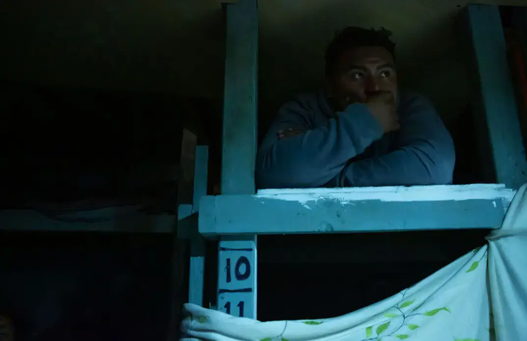 Nelson rests in his bunk at a Tijuana shelter for migrants, asylum-seekers and deported people. The shelter supports individuals and families from Afghanistan, Venezuela, Central America and the Middle East, says Hugo Castro, of the nonprofit group Border Angels. Image by Erika Schultz. Mexico, 2019.