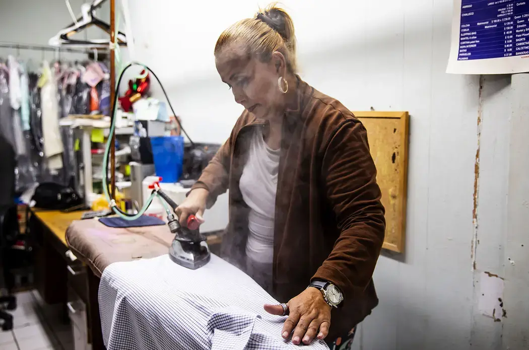 Daysi works ironing clothes at a laundry in Tijuana and her son, Jimmy, 12, sells shrimp at the beach near the U.S. border. Image by Erika Schultz. Mexico, 2019.