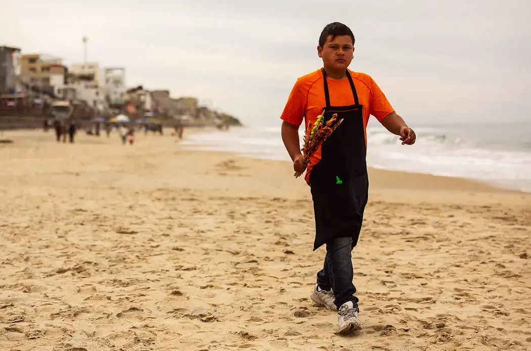 Daysi works ironing clothes at a laundry in Tijuana and her son, Jimmy, 12, sells shrimp at the beach near the U.S. border. Image by Erika Schultz. Mexico, 2019.