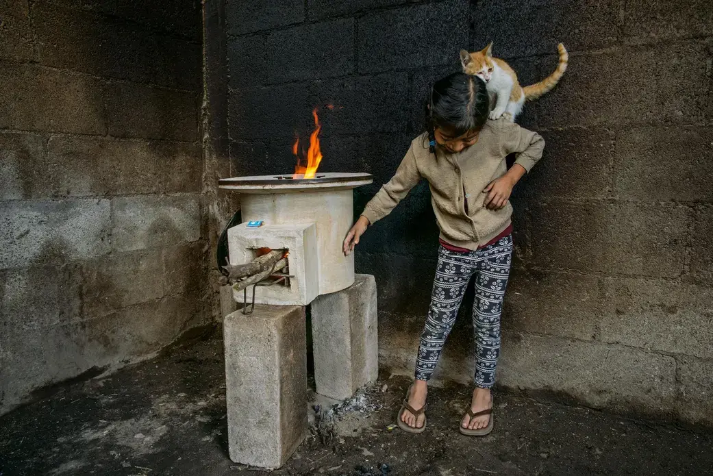 Tania López, seven, plays with her cat in a room whose walls were blackened by an old open fire; the new stove, provided by StoveTeam International, is efficient and safe to touch. Image by Lynn Johnson. Guatemala, 2017.