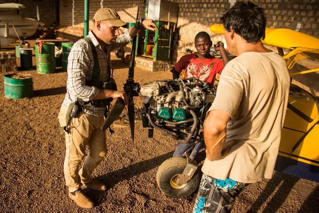 Simpson, the park manager, (left) inspects a bush plane undergoing repairs inside a hanger at Chinko. Image by Jack Losh. Central African Republic, 2018.