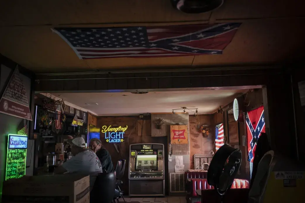 People sit in a bar decorated with an American flag and Confederate flags before noon in Meridian, Miss. Image by Wong Maye-E / The Associated Press. United States, 2020.